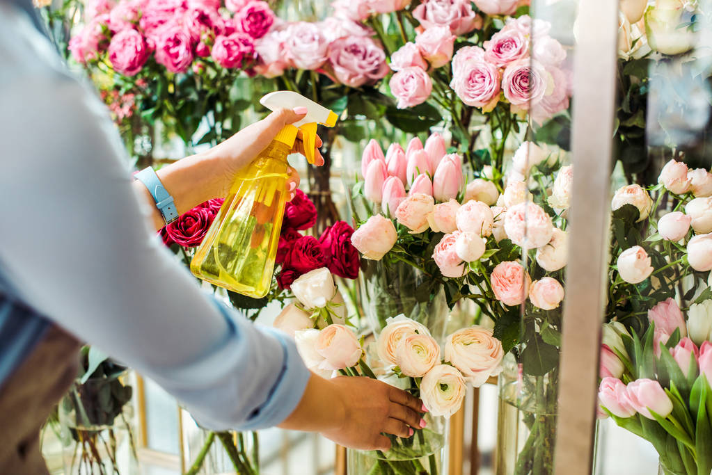 Ausgeschnittene Ansicht einer Blumenhändlerin, die Blumen mit Sprühflasche in Blumenladen sprüht - Foto, Bild