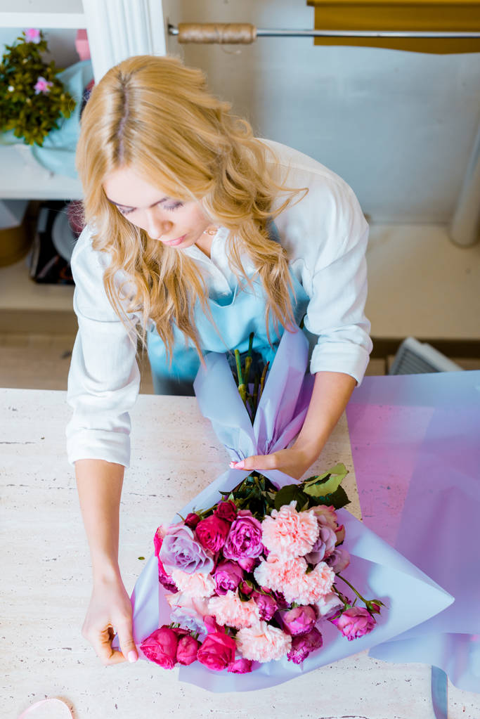 красивая женщина-флористка устраивает букет с розами и гвоздиками в цветочном магазине
 - Фото, изображение