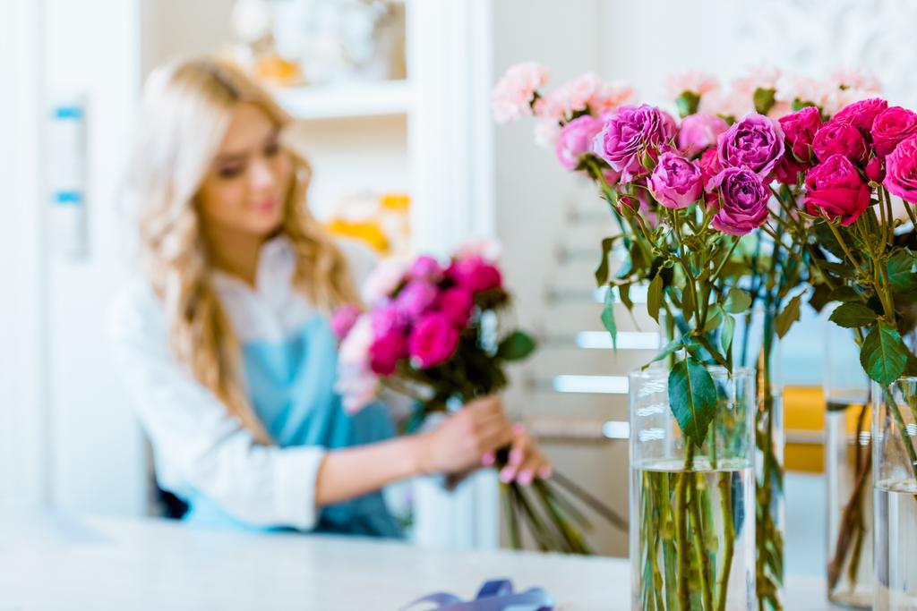 селективный фокус роз с женским флористом, расставляющих букет в цветочном магазине на заднем плане
 - Фото, изображение