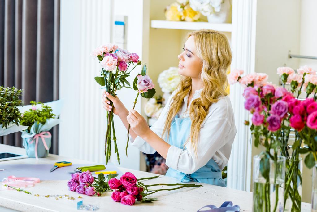 bella fiorista femminile in grembiule organizzare bouquet con rose in negozio di fiori
  - Foto, immagini
