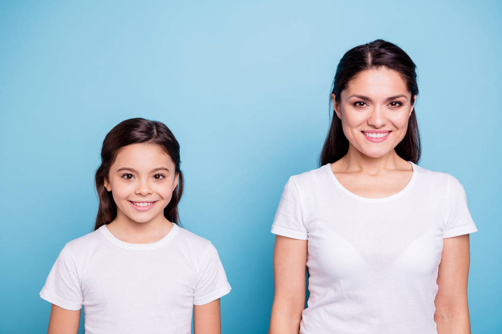Close up photo two people brown haired mum and small daughter standing straight looking to camera wearing white t-shirts isolated on bright blue background - Photo, Image