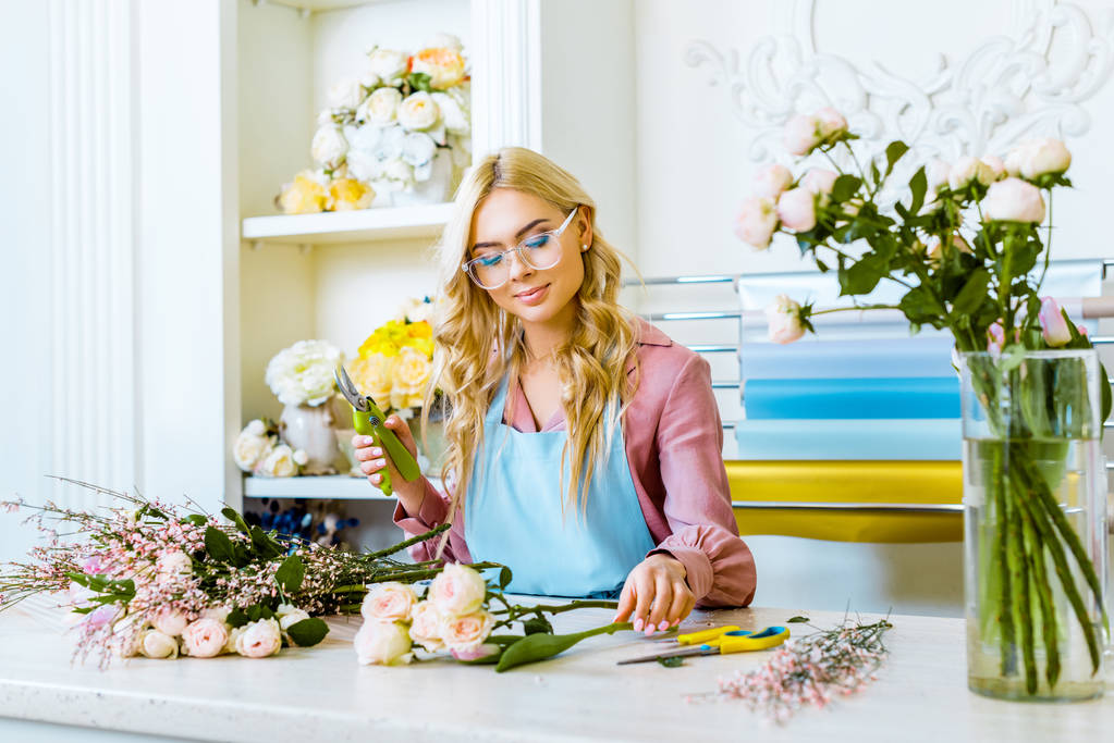 bela florista feminina em óculos arranjando buquê e segurando poda na loja de flores
 - Foto, Imagem