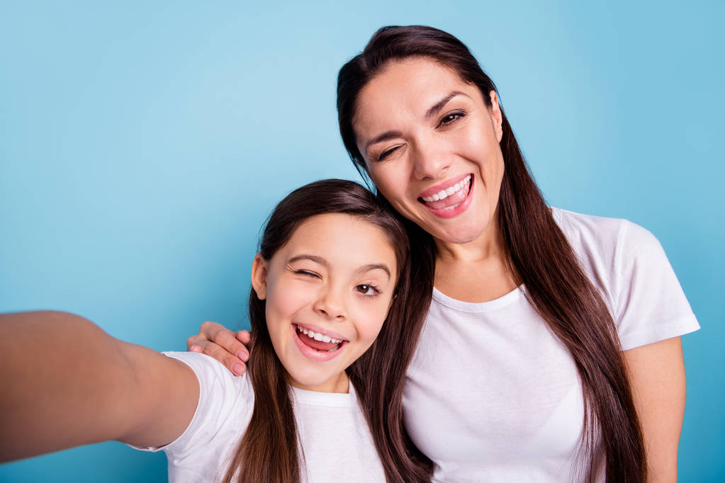 Lähikuva valokuva hurrata kauniita kaksi ihmistä ruskea tukkainen äiti pieni tytär tehdä ottaa selfietä suussa nauraa naurua flirttaileva silmänisku kulumista valkoinen t-paitoja eristetty kirkkaan sininen tausta
 - Valokuva, kuva