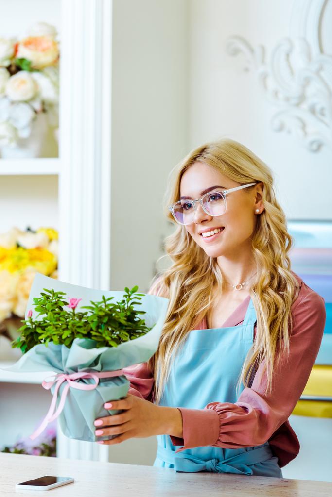 beautiful smiling female florist in glasses presenting bouquet in flower shop - Photo, Image