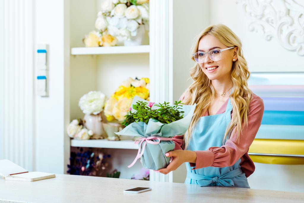 красивая улыбающаяся цветочница в очках, преподносящая букет в цветочном магазине
 - Фото, изображение