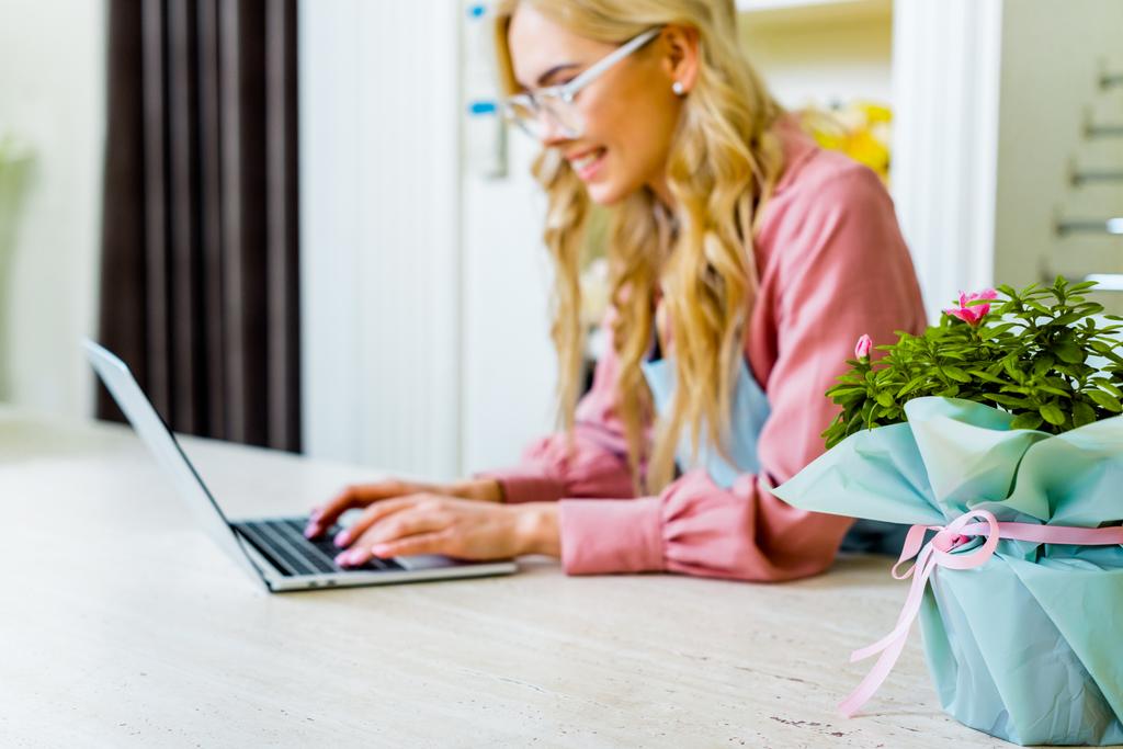 selective focus of floral bouquet with female florist using laptop in flower shop on background  - Photo, Image