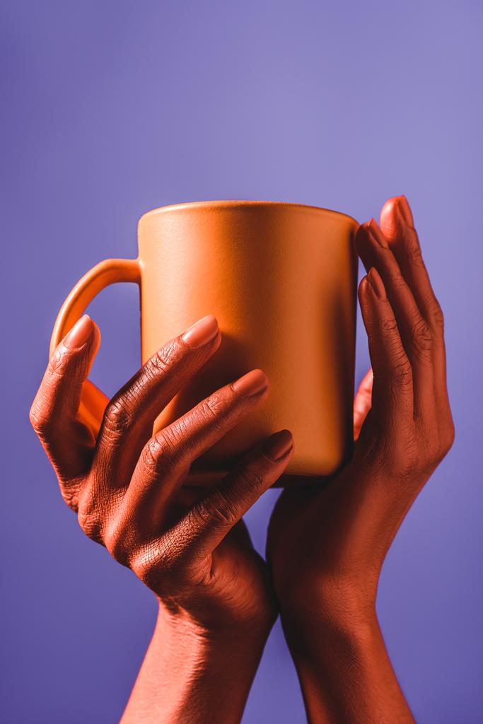 partial view of woman with coral colored hands holding coral coffee cup on violet background,  color of 2019 concept - Photo, Image