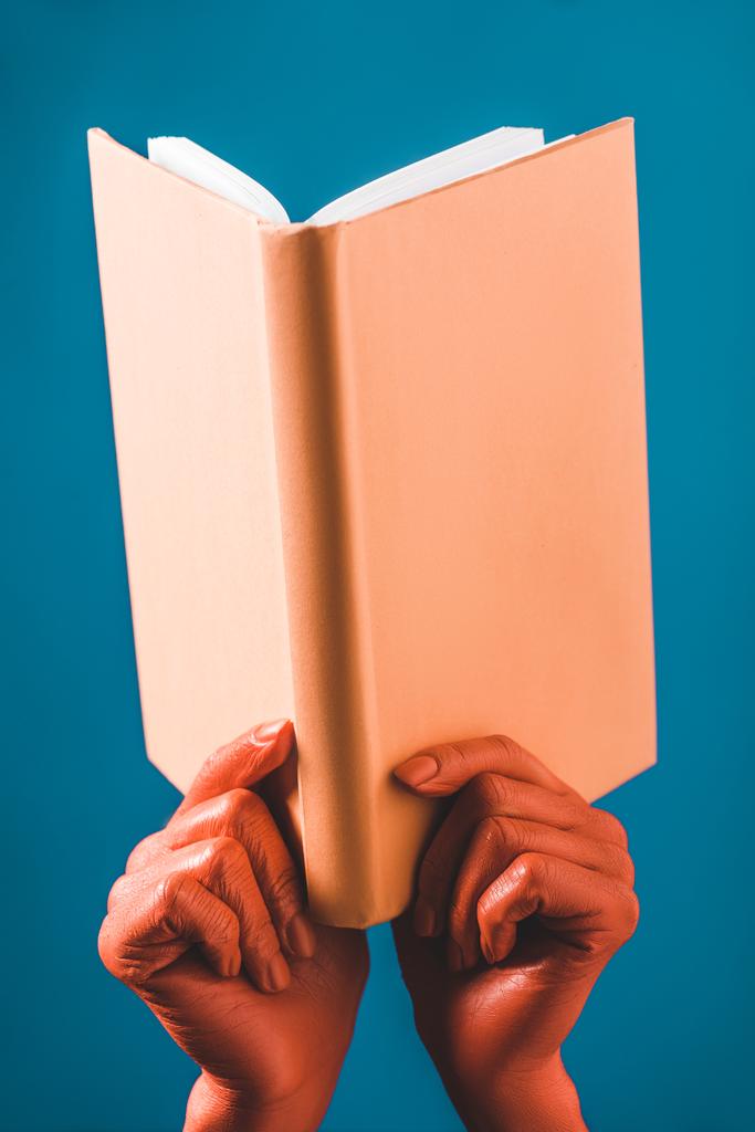 cropped view of woman with coral colored hands holding coral book on blue background, color of 2019 concept - Photo, Image