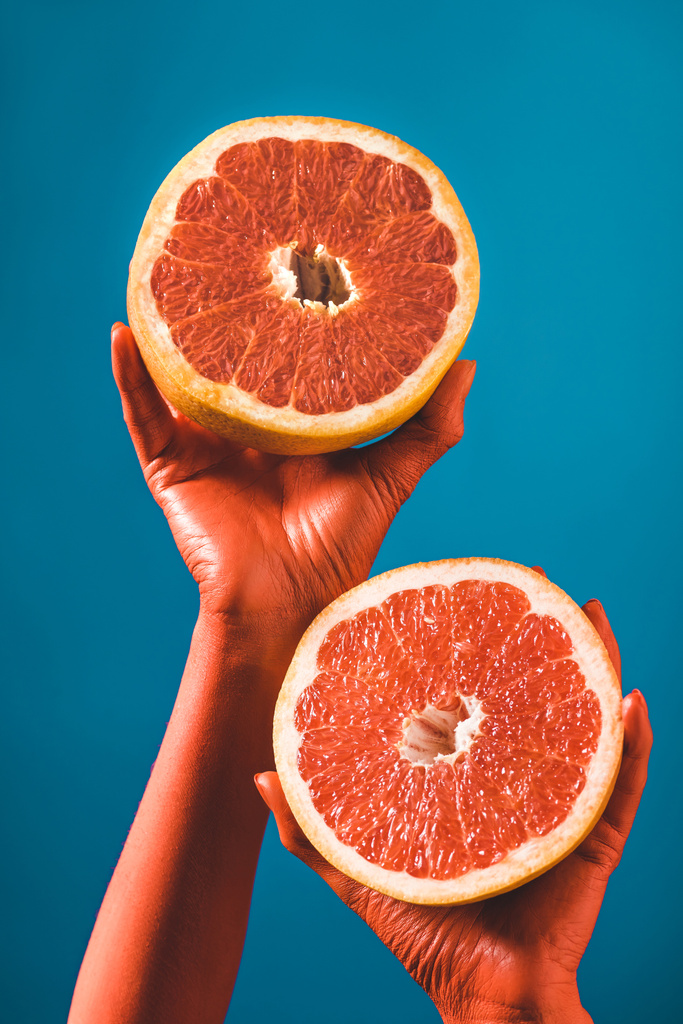 bijgesneden beeld van vrouw met grapefruit helften in koraal gekleurde handen op blauwe achtergrond, kleur van 2019 concept  - Foto, afbeelding