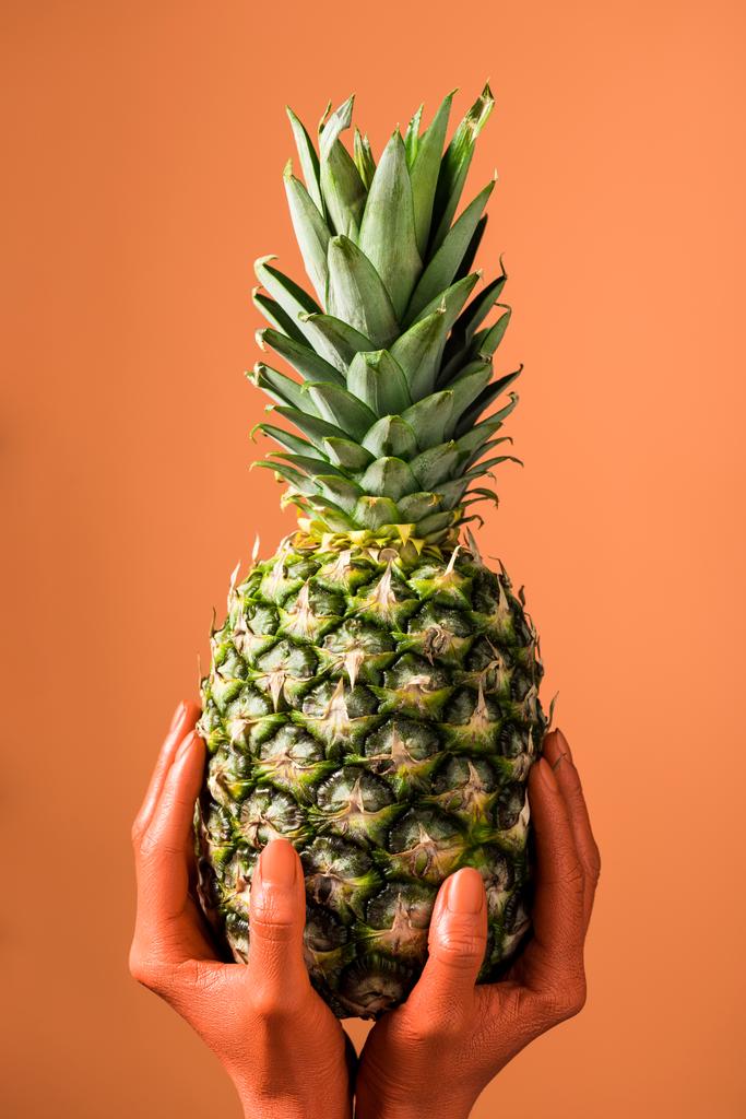 Teilansicht der korallenfarbenen weiblichen Hände mit Ananasfrüchten auf korallenfarbenem Hintergrund, Farbe des Konzepts 2019 - Foto, Bild