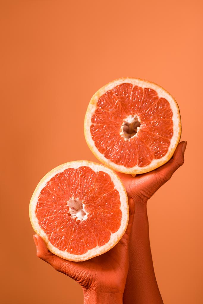 partial view of coral colored female hands with grapefruit halves on coral background, color of 2019 concept - Photo, Image