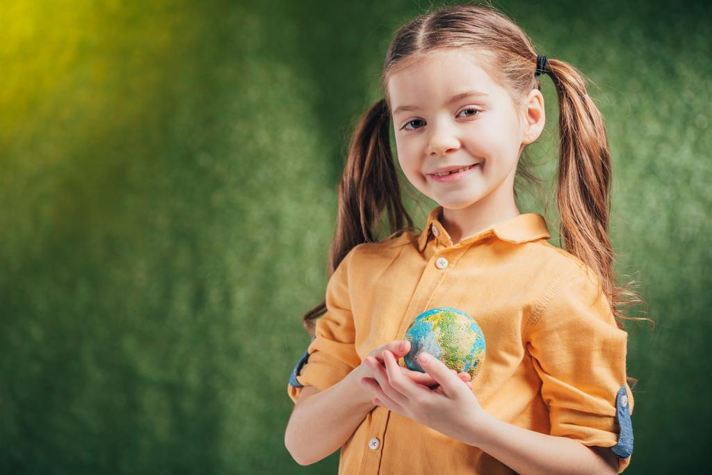arka plan, dünya gün kavramı küre modeli kalp yakın tutarak sevimli gülümseyen çocuk bulanık - Fotoğraf, Görsel