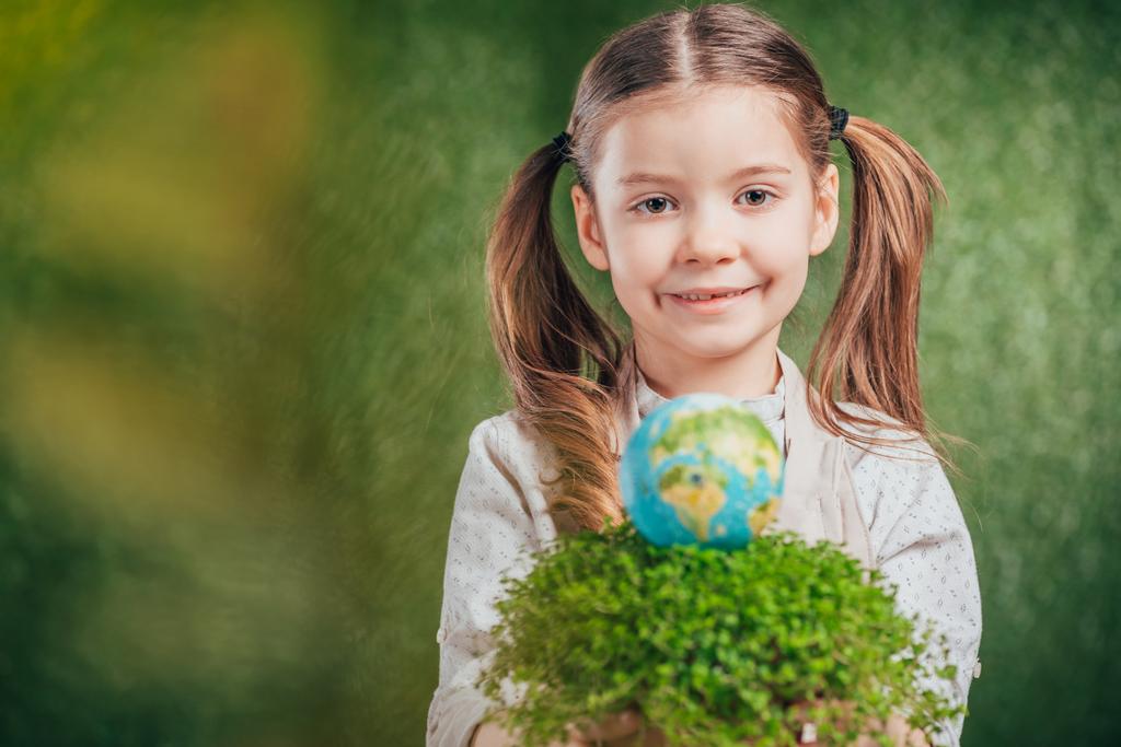 επιλεκτική εστίαση του χαμογελαστού παιδιού με λουλούδι ποτ και globe μοντέλο σε θολή φόντο, έννοια την ημέρα της γης - Φωτογραφία, εικόνα