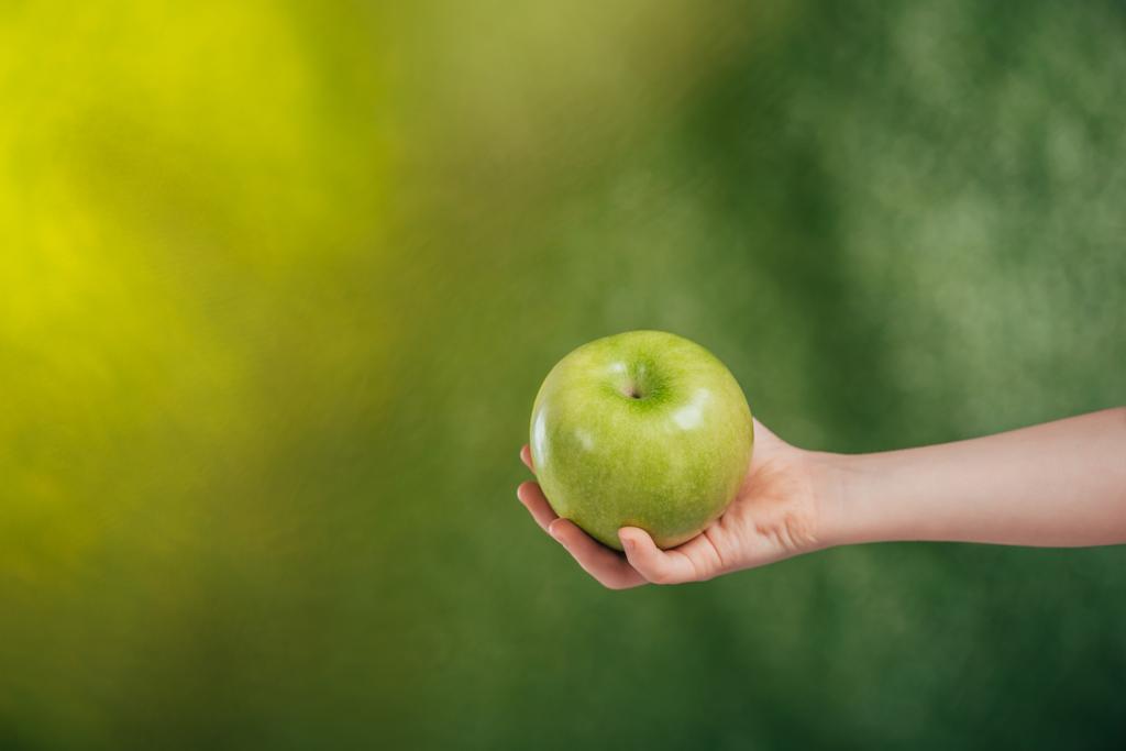 partial view of child hand with apple on blurred background, earth day concept - Photo, Image