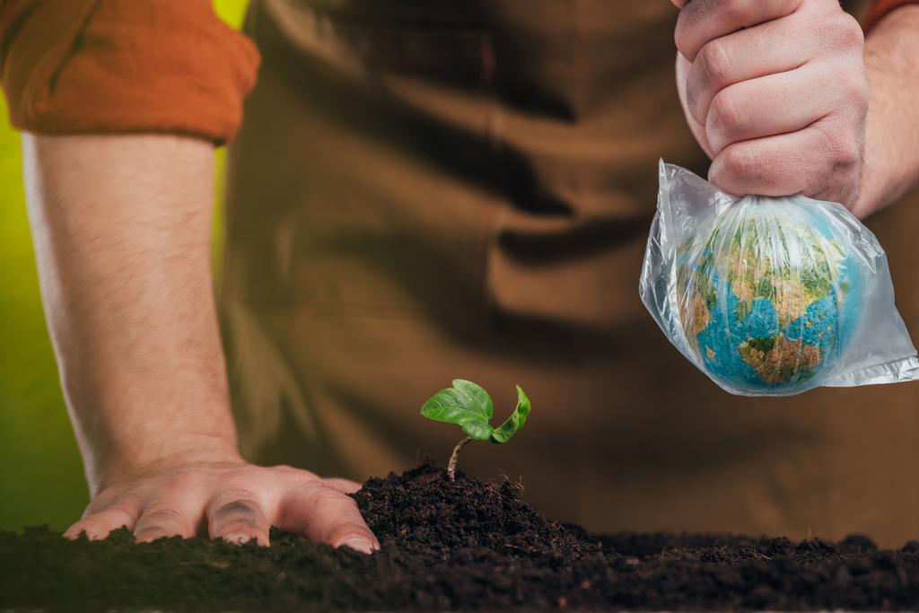 foco seletivo do homem plantando planta jovem e segurando modelo globo em saco de plástico no fundo borrado, conceito de dia de terra
 - Foto, Imagem
