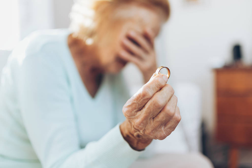 Herzzerreißende ältere Frau hält ihren Ehering in der Hand - Foto, Bild