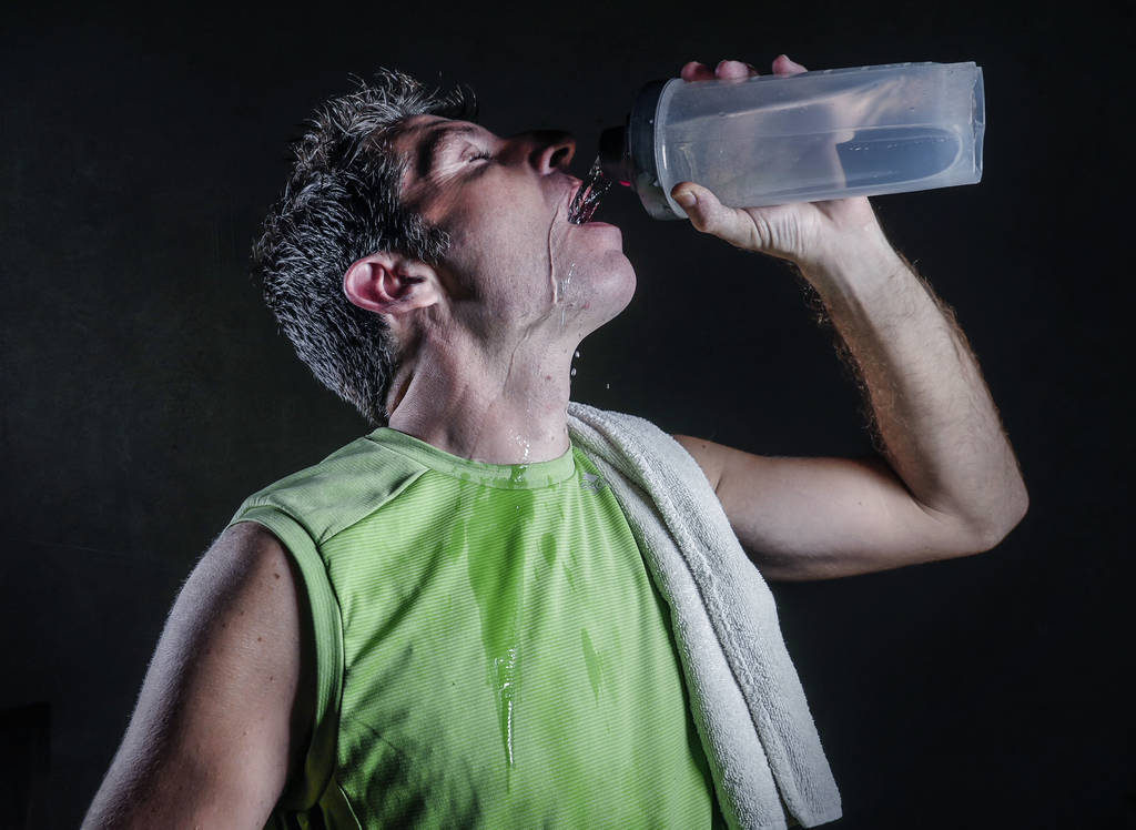 jovem homem esportivo cansado e exausto com toalha em seu ombro suado bebendo garrafa de água após o treino duro e treinamento de fitness isolado em fundo escuro no conceito de estilo de vida saudável
 - Foto, Imagem