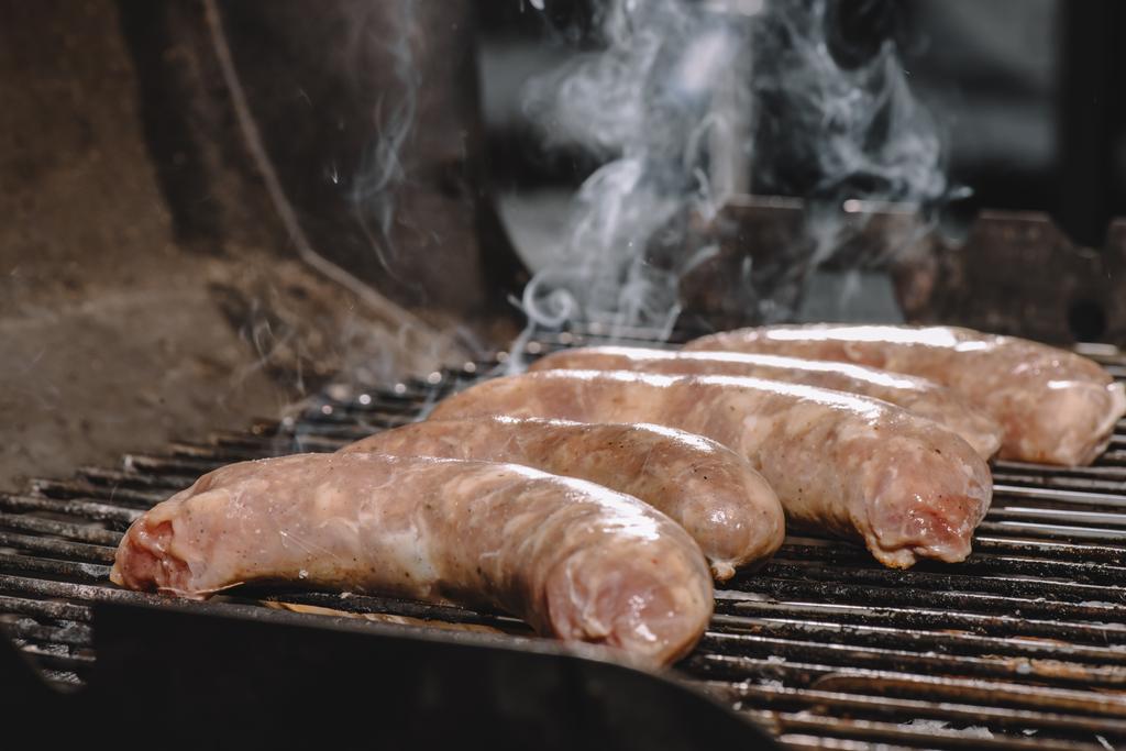 selective focus of raw sausages cooking on bbq grill with smoke - Photo, Image