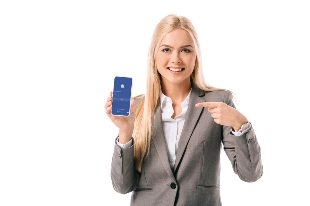 sonriente mujer de negocios apuntando al teléfono inteligente con aplicación de facebook, aislado en blanco
 - Foto, imagen