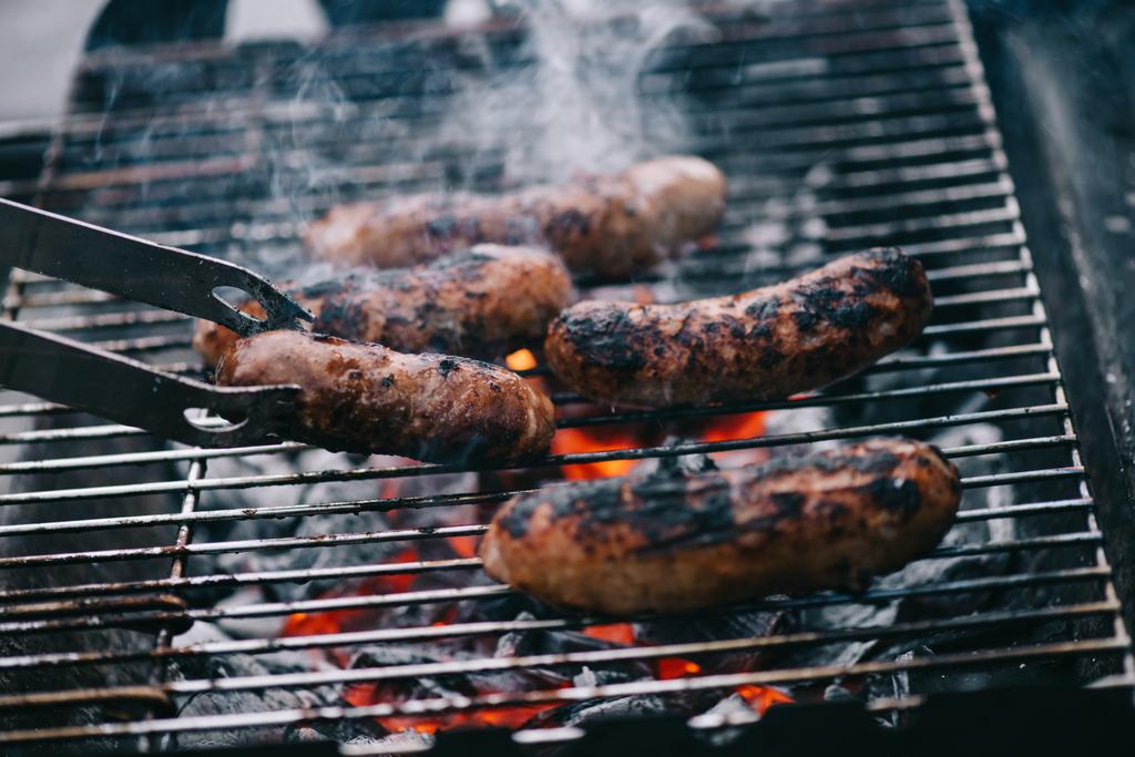 foyer sélectif de pinces à épiler près de saucisses grillées sur le barbecue
 - Photo, image