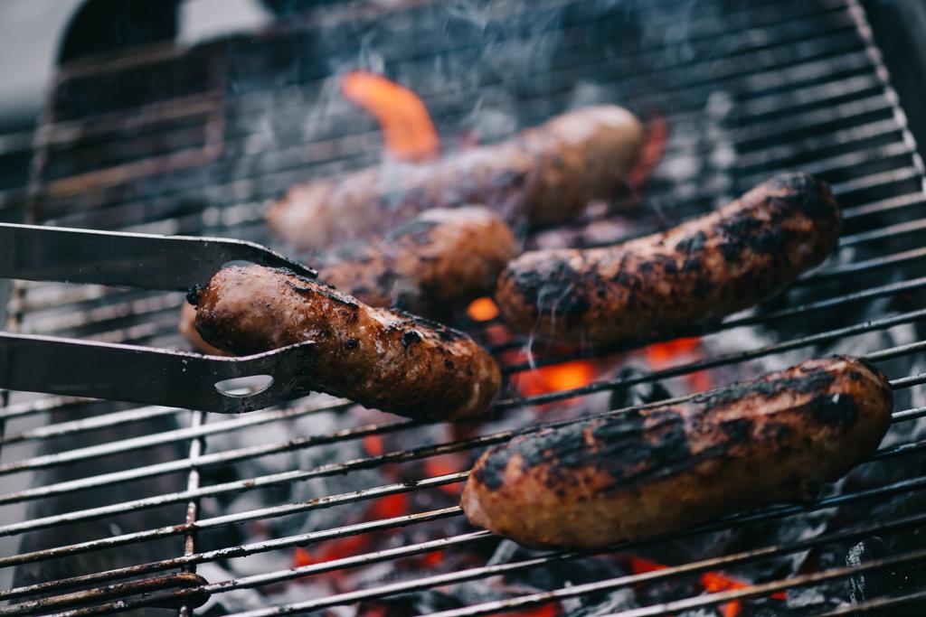 selective focus of tweezers with grilled sausage on barbecue  - Photo, Image