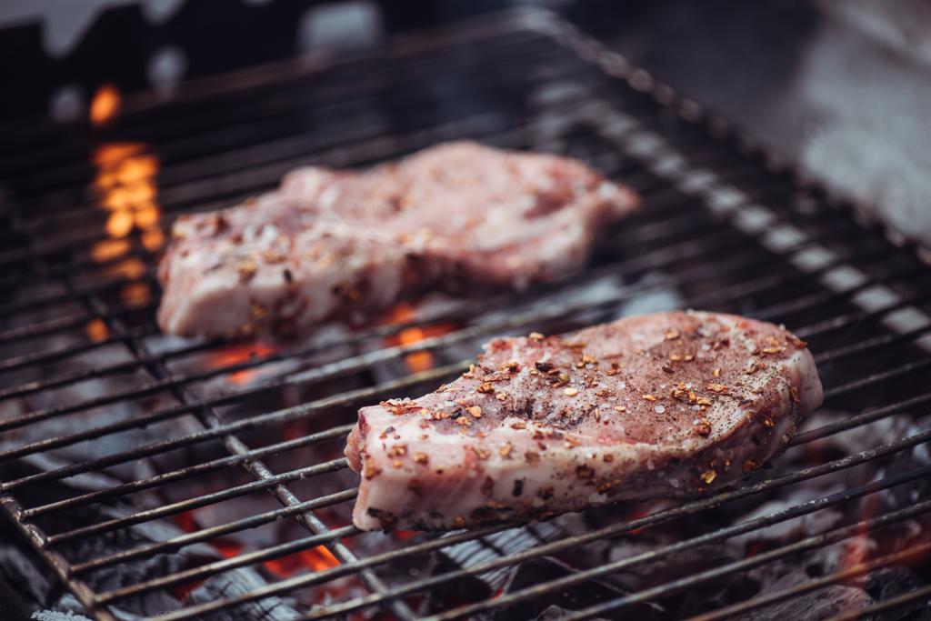 selective focus of juicy raw steaks grilling on barbecue grid - Photo, Image