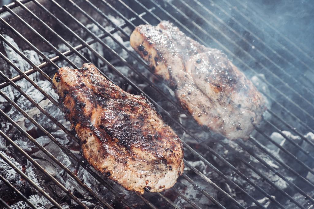 selektiver Fokus auf saftige Steaks, die auf heißen Kohlen mit Rauch grillen - Foto, Bild