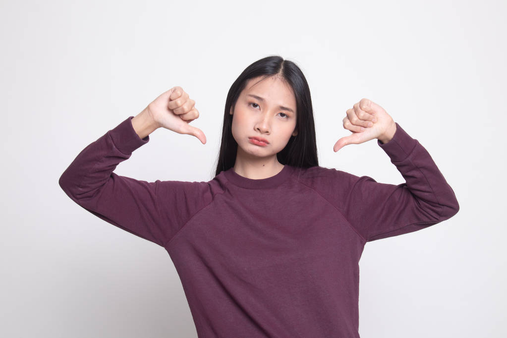 unglückliche asiatische Mädchen zeigen Daumen nach unten mit beiden Händen auf weißem Hintergrund - Foto, Bild