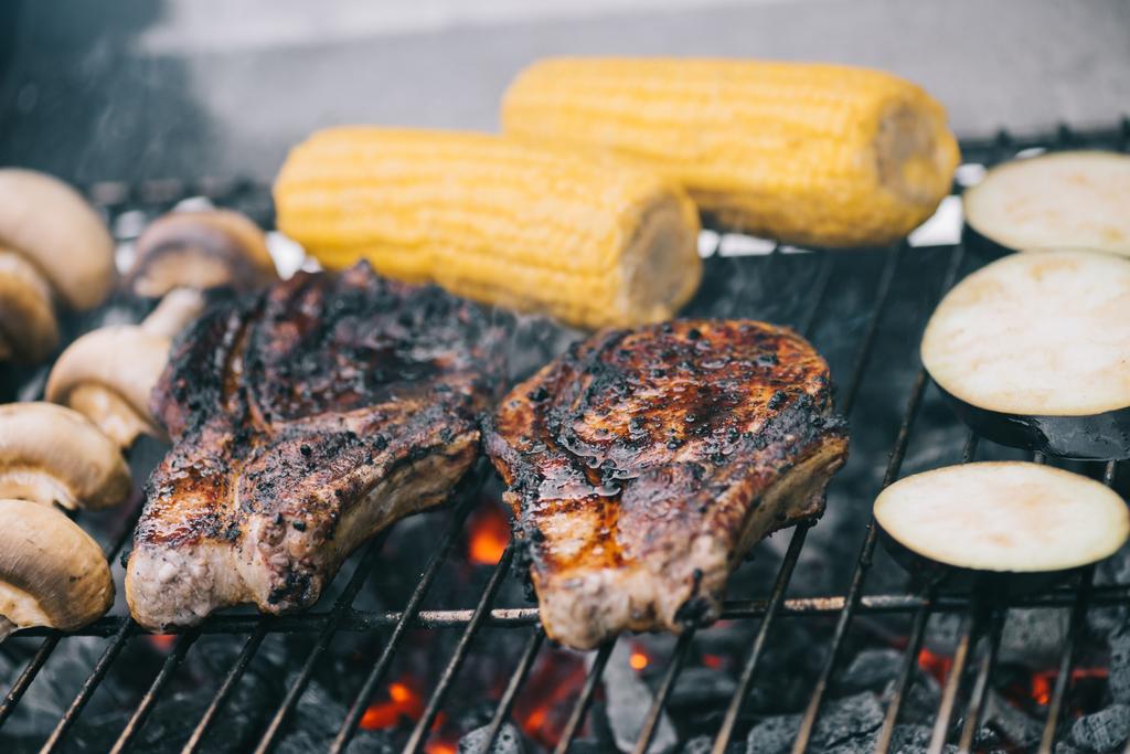 selective focus of tasty steaks grilling on bbq grid with mushrooms, corn and sliced eggplant - Photo, Image