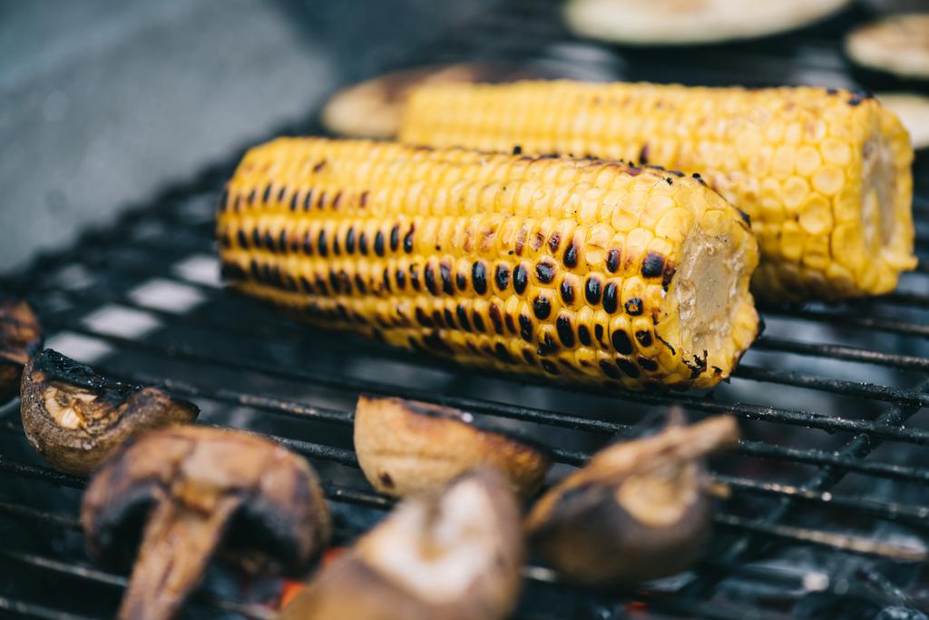 selectieve aandacht van gele maïs met korst en paddestoelen grillen op de barbecue raster - Foto, afbeelding