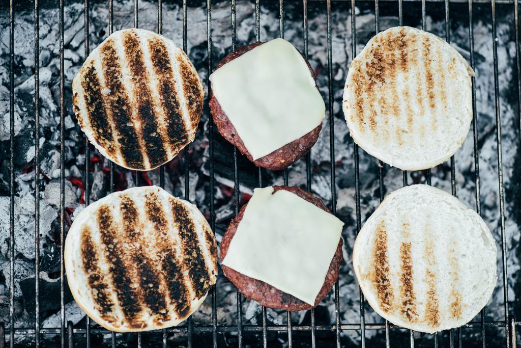 bovenaanzicht van heerlijke verse hamburgers ingrediënten grillen op de BBQ-rooster - Foto, afbeelding