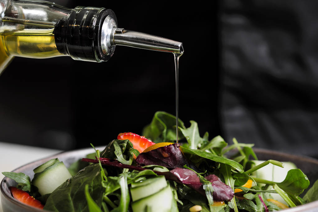 Ruoanlaitto salaatti kokki keittiössä ravintolassa. Kastelu oliiviöljyä pullosta annostelija
. - Valokuva, kuva