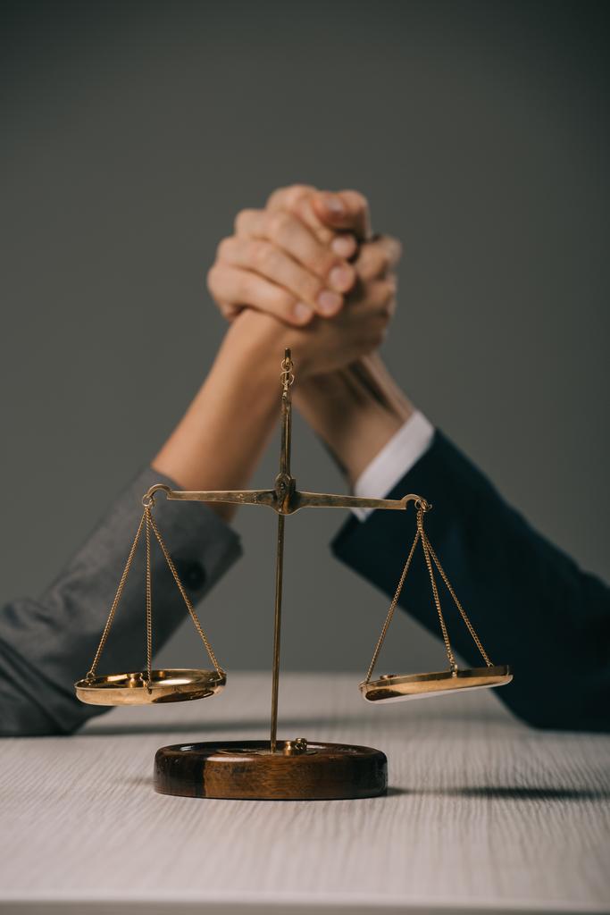 селективный фокус деловых коллег вооружает нищего на деревянном столе с весами правосудия на сером
 - Фото, изображение