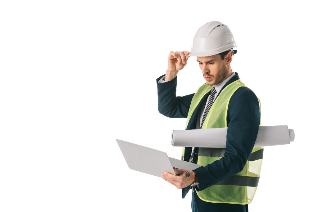 αρσενικό μηχανικός hardhat και ασφάλεια vest κρατώντας blueprint και χρήση φορητού υπολογιστή, απομονώνονται σε λευκό - Φωτογραφία, εικόνα