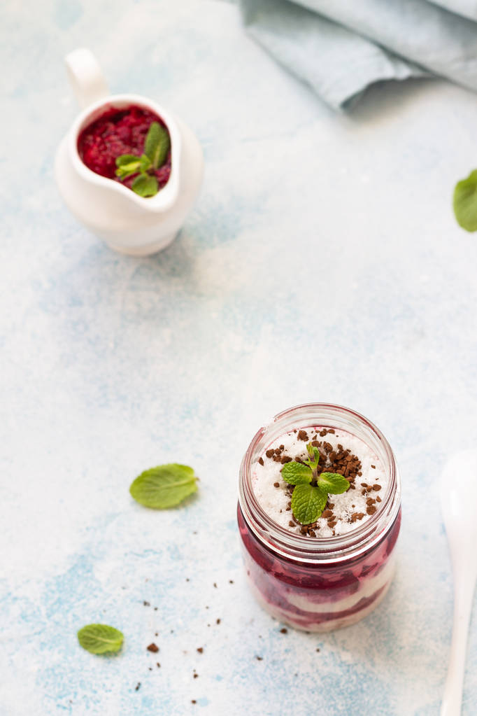 Tasty cottage cheese parfait with raspberry sauce and mint in a glass jar. Diet dessert. Light grey stone concrete background. Copy space. - Photo, Image
