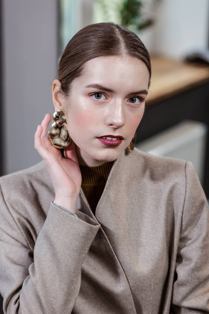 Mooie langharige mooie vrouw in een stijlvol jasje te tonen haar earring - Foto, afbeelding