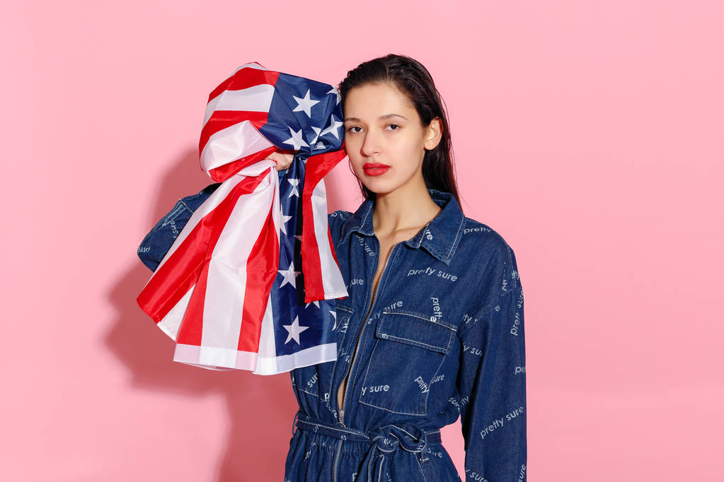Büszke női sportoló portréja csomagolva amerikai zászló rózsaszín háttér. Izmos fiatal nő magabiztosan nézi a kamera. női tiltakozott az egyenlőség és a nők szerepének erősítése - Fotó, kép