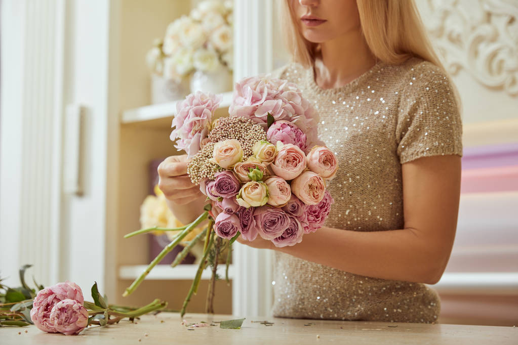 valikoiva painopiste kukkakauppias tekee kimpun ruusuja ja pioneja työtilassa
 - Valokuva, kuva