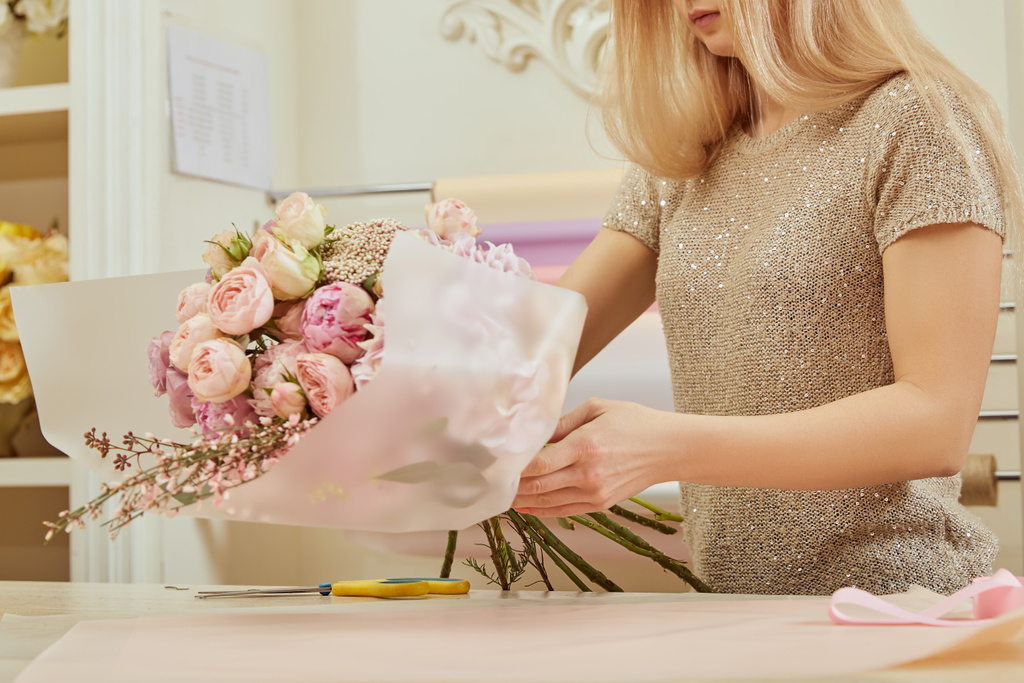 vista parziale del fiorista che avvolge bouquet di rose e peonie sullo spazio di lavoro
 - Foto, immagini