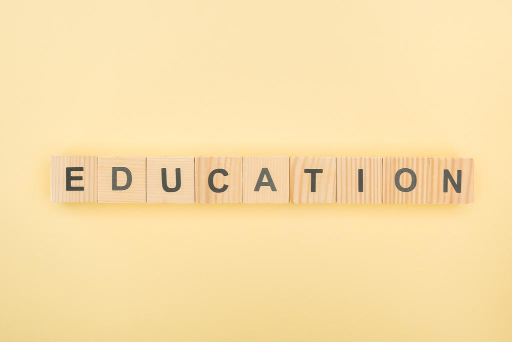 Draufsicht auf Bildungsschriftzug aus Holzwürfeln auf gelbem Hintergrund - Foto, Bild