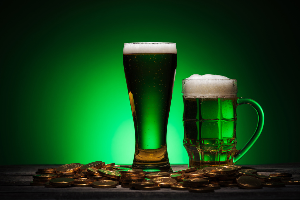 glasses of green ale near golden coins on green background - Photo, Image