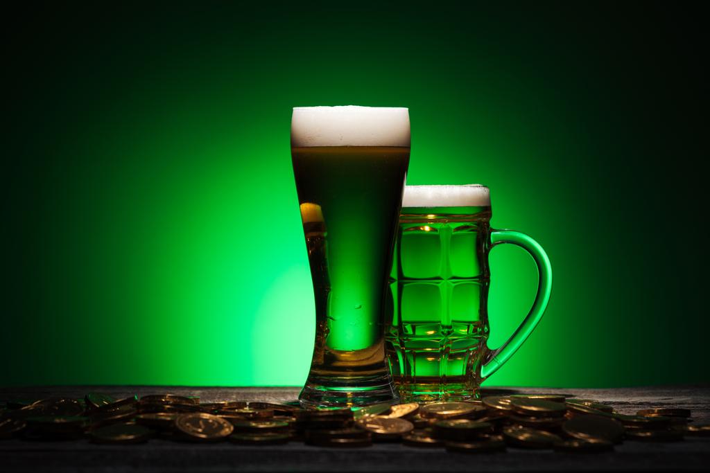 glasses of irish beer standing near golden coins on wooden table on green background - Photo, Image