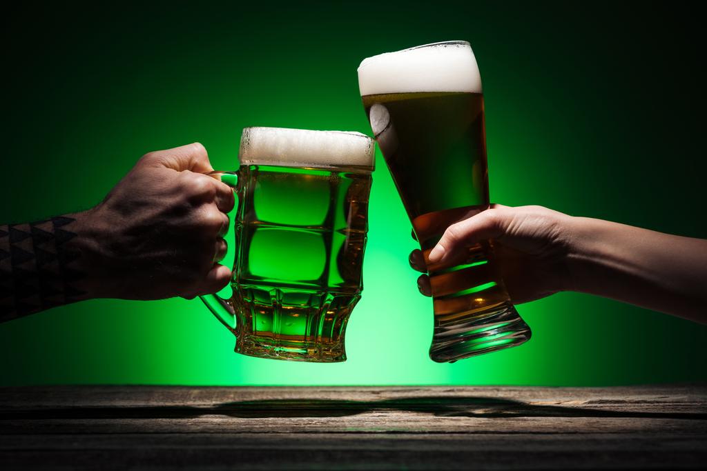 oříznutý pohled mužů cinkání sklenic piva na zeleném pozadí - Fotografie, Obrázek