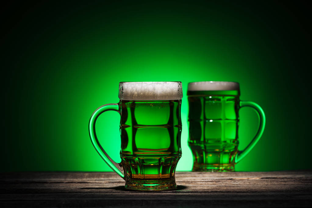copos de cerveja em pé sobre mesa de madeira sobre fundo verde
 - Foto, Imagem
