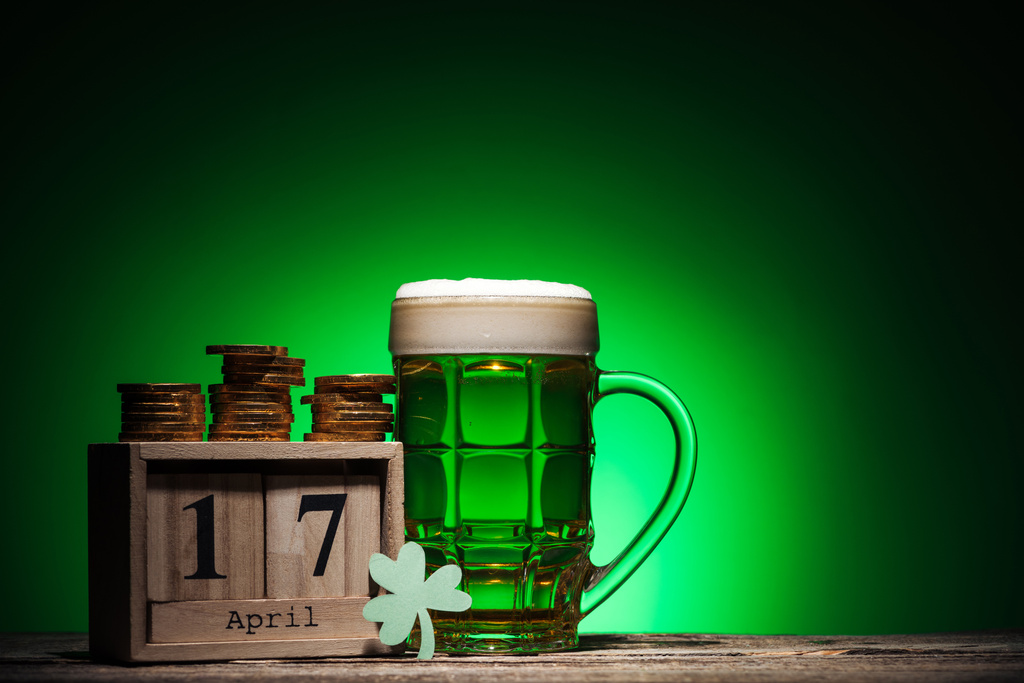 pohár zöld ír ale közelében arany érmék és zöld háttér kocka naptár - Fotó, kép