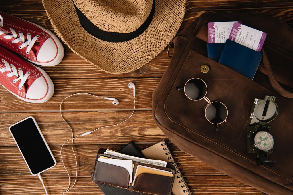 vista superior del smartphone con auriculares, pasaportes con entradas y accesorios con camas en superficie de madera
 - Foto, imagen