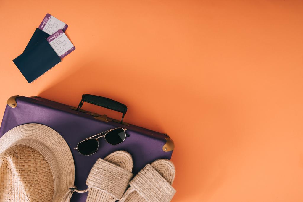 bovenaanzicht van zomer accessoires op reistas met paspoorten en tickets op oranje achtergrond - Foto, afbeelding