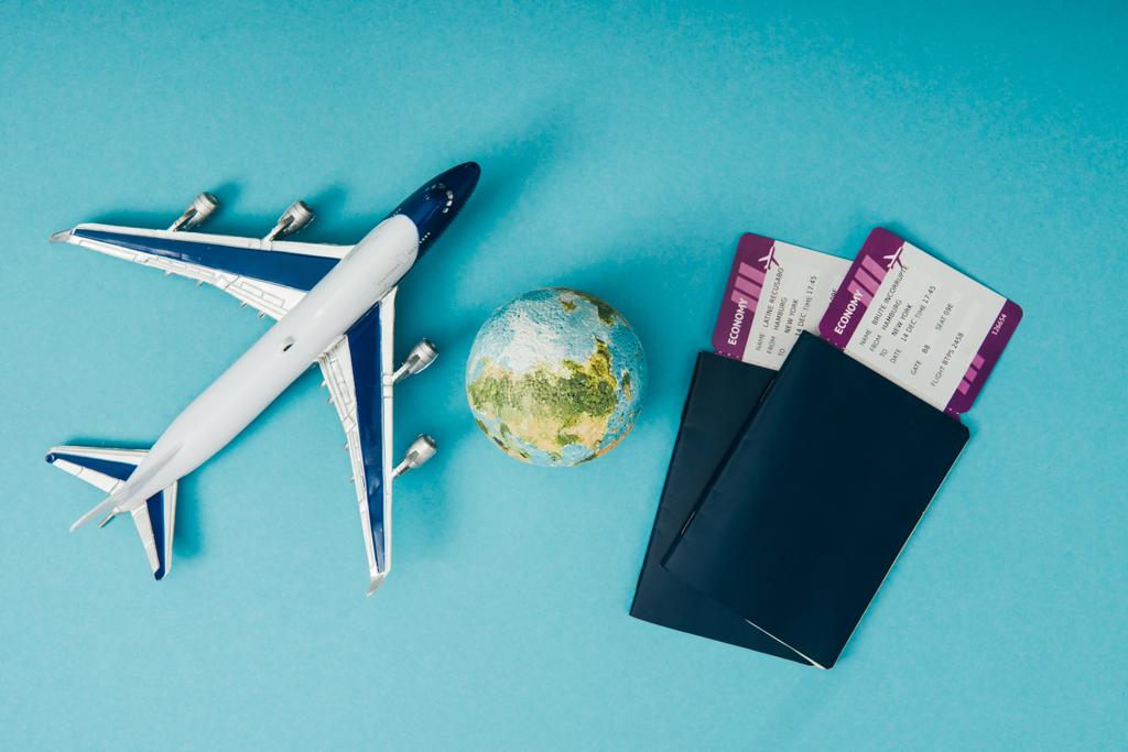 Küre ve uçak modelleri, mavi zemin üzerine biletli pasaportlar üstten görünüm - Fotoğraf, Görsel