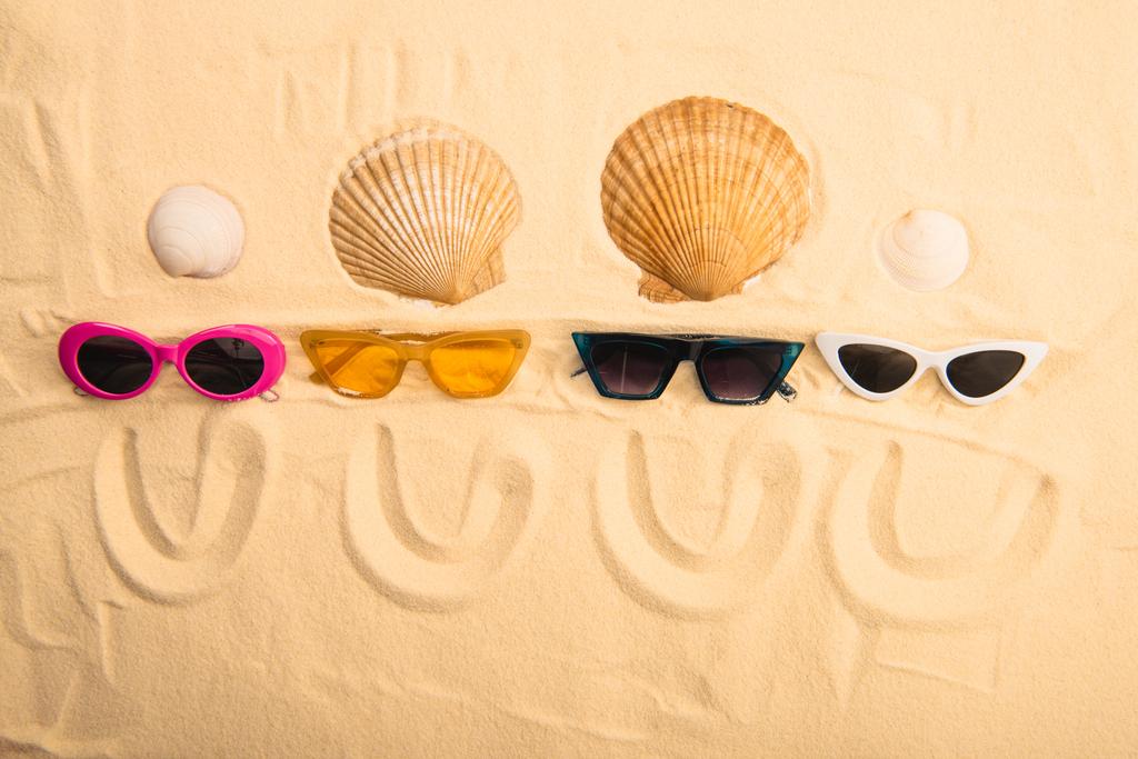 Sonnenbrille und Muscheln von oben mit einem Lächeln auf Sand - Foto, Bild