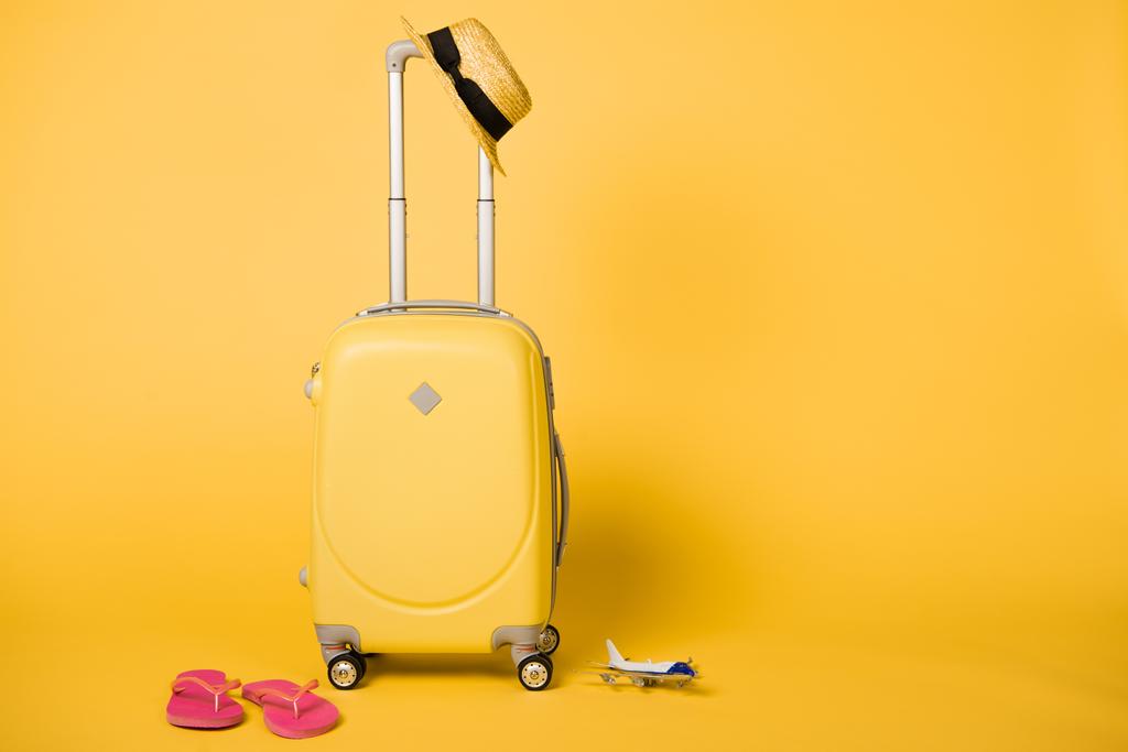 heldere gele reistas, stro hoed, roze slippers en vlak model op gele achtergrond - Foto, afbeelding